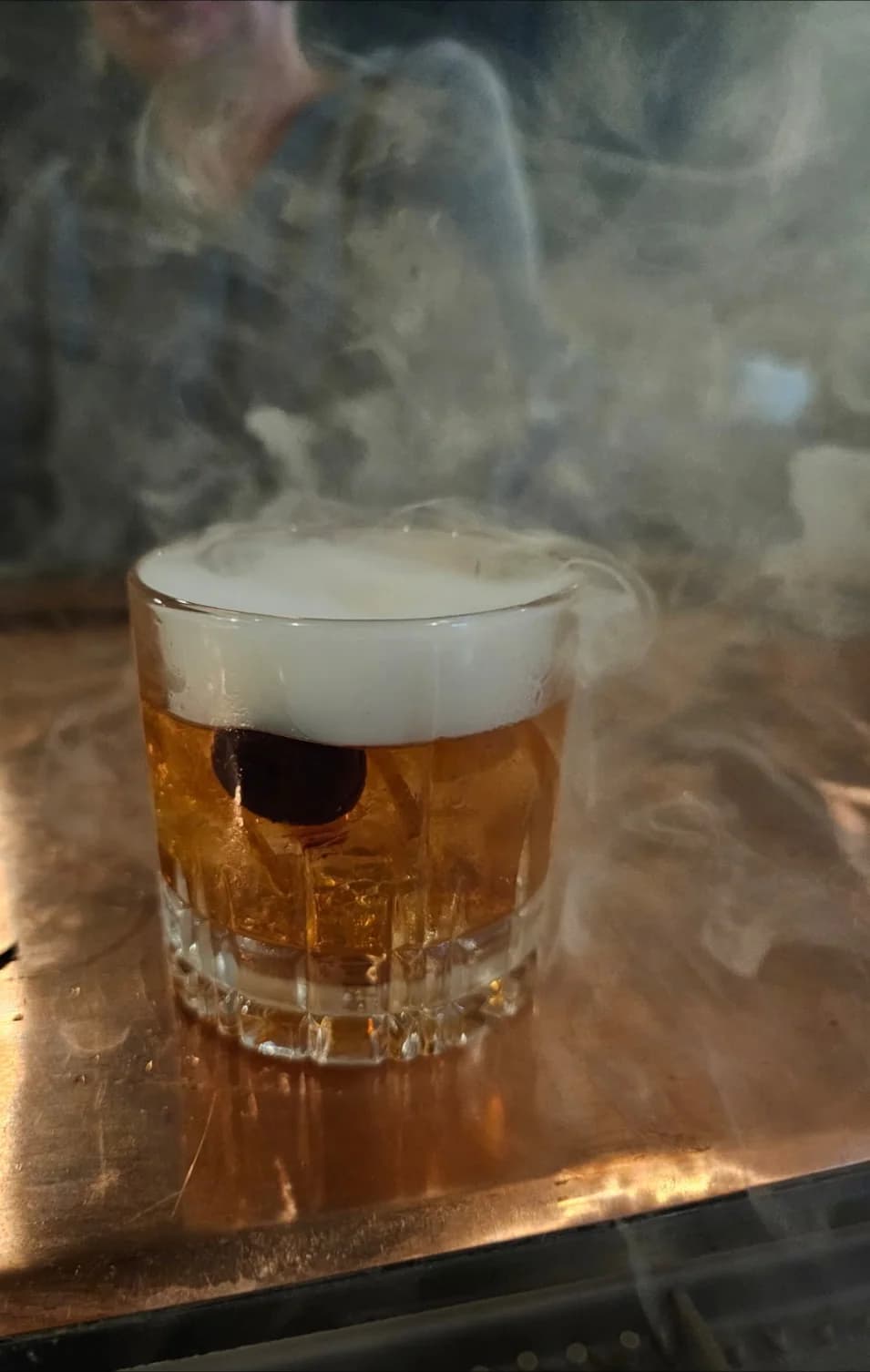 An amber cocktail surrounded by smoke on the copper bar at SPUR